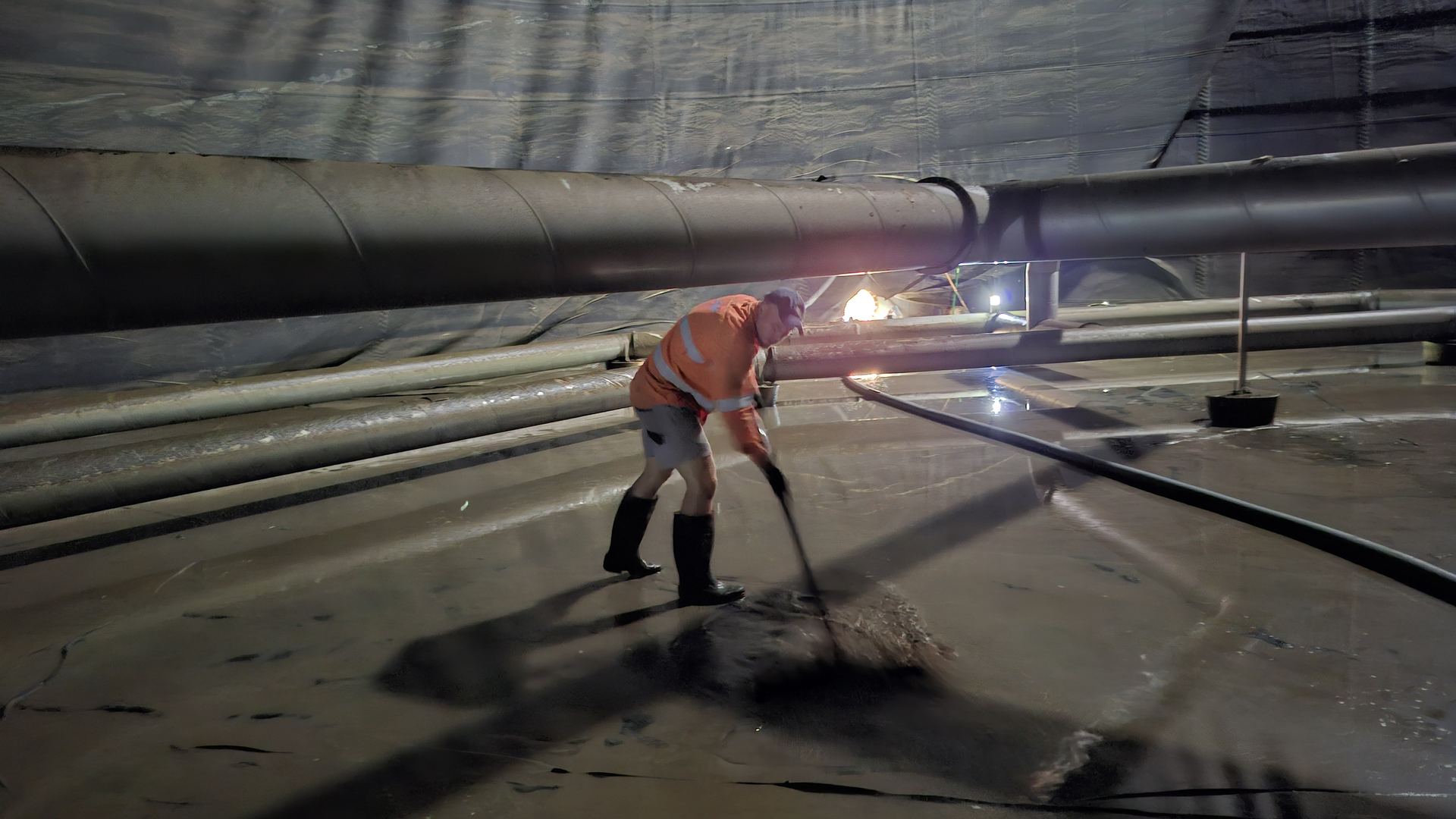 Worker clearing sludge from the floor inside a drained storage tank
